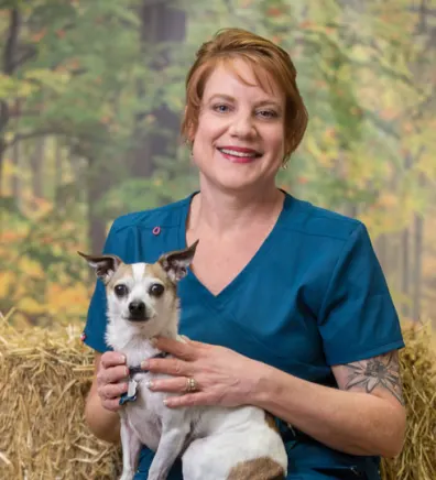 Linda dressed in blue scrubs holding a small tan and white dog
